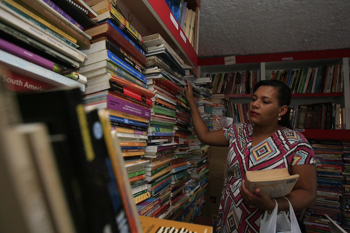 Mulher organizando estante de livros | Foto: Joa Souza/Shutterstock
